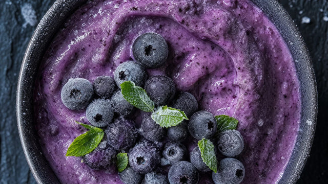 Dunkle Schale mit cremiger Heidelbeer-Frozen-Bowl von oben, gefrorene Heidelbeeren und Minze, Kondenswasser am Rand