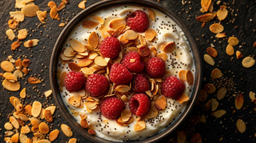 Dunkle Schale mit cremiger Proteinbasis, goldene geröstete Mandelblättchen und frische Himbeeren darüber, von oben fotografiert