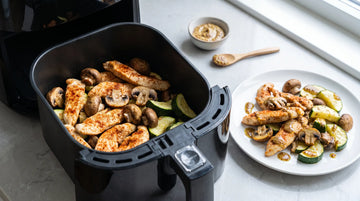 Putenstreifen mit Champignons und Zucchini im offenen Airfryer-Korb, daneben ein fertiger Teller