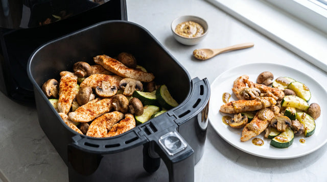 Putenstreifen mit Champignons und Zucchini im offenen Airfryer-Korb, daneben ein fertiger Teller