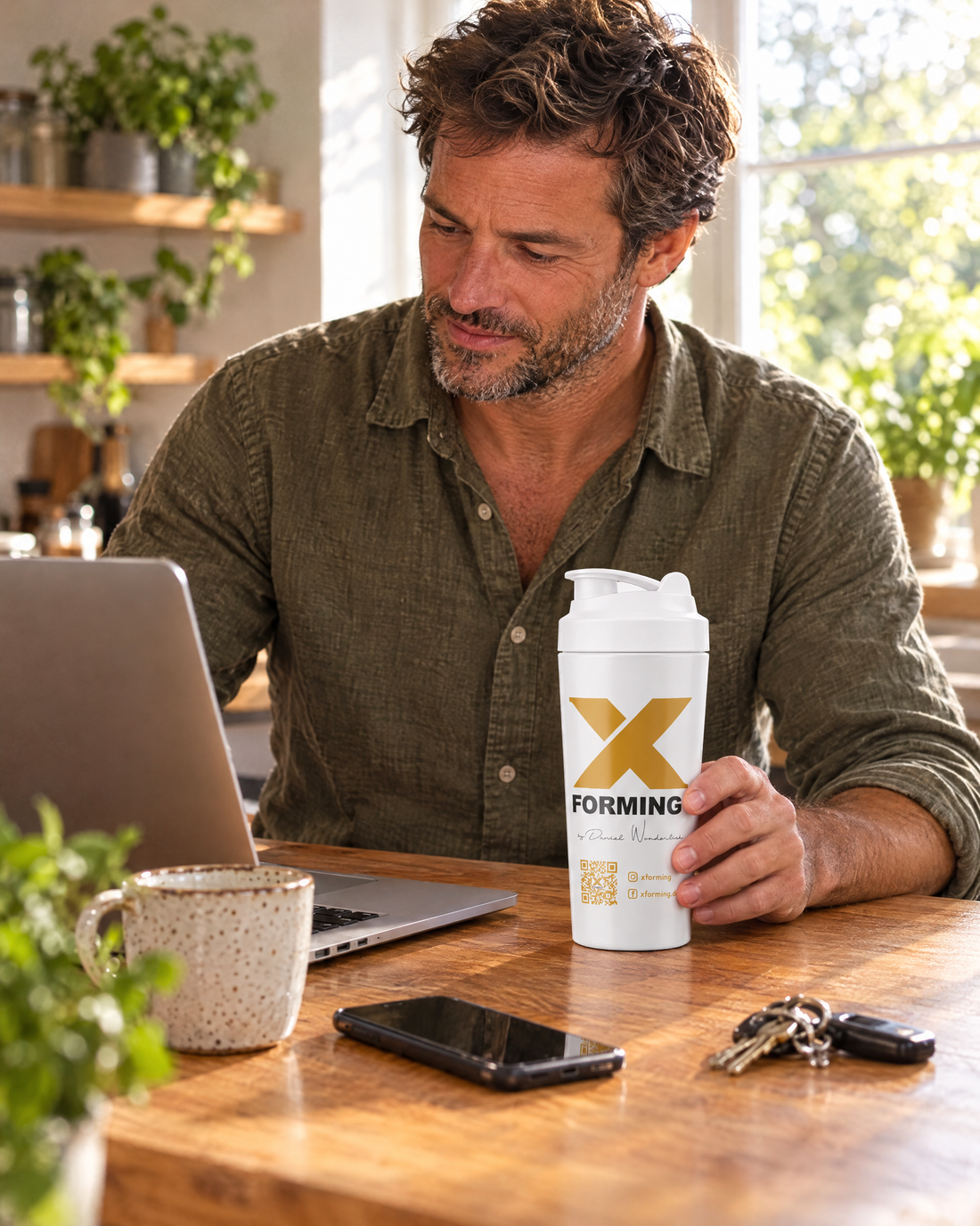 Mann am Morgen am Laptop, der X-FORMING Shaker steht griffbereit daneben